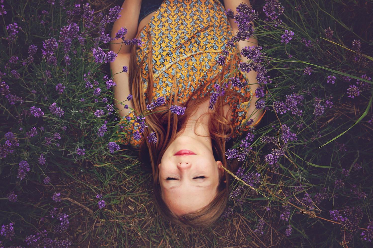 Woman lying on the ground with her eyes closed on grass among purple flowers